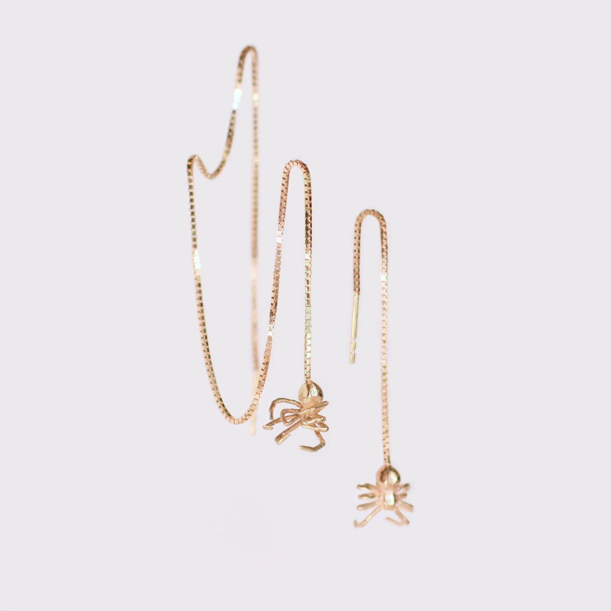 Two gold threader earrings with a spider charm at the end of each